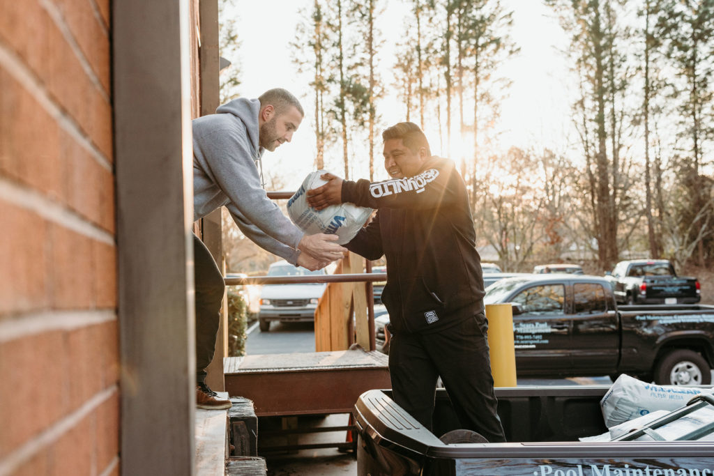 two guys handing each other pool chemicals